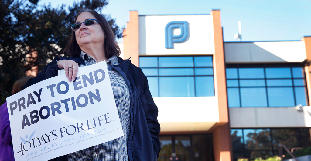 An anti-abortion protester holds a vigil outside of a Planned Parenthood office Holding a sign that says "Prayed to end abortion. 40 Days For Life."