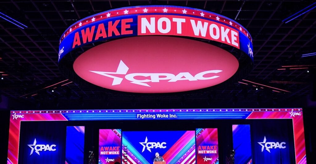 A sign that says "AWAKE NOT WOKE" hangs over the stage before the Conservative Political Action Conference meeting.