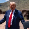 Donald Trump in a blue suit and red tie outside at the US-Mexico border.