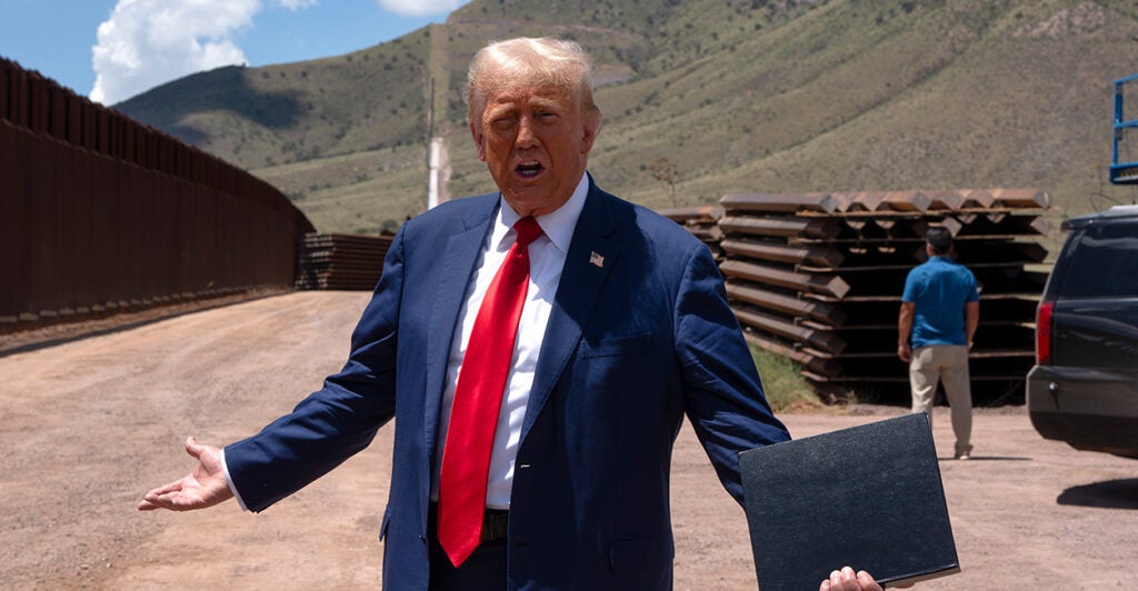 Donald Trump in a blue suit and red tie outside at the US-Mexico border.