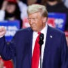 Donald Trump smiles and raises his fist in a blue suit with a red tie