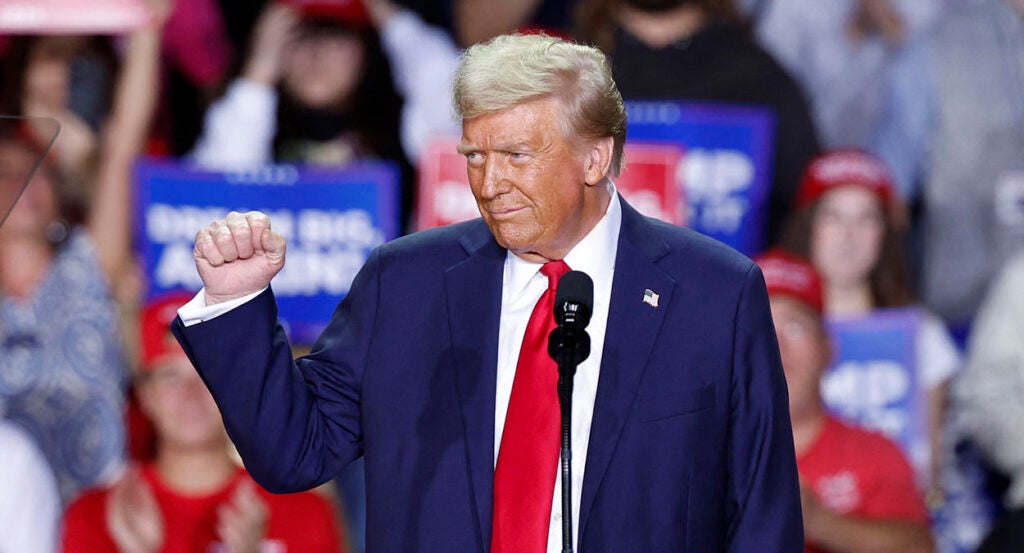 Donald Trump smiles and raises his fist in a blue suit with a red tie