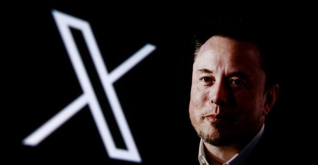 Elon Musk is posing next to the X logo, what he rebranded Twitter after he bought it.