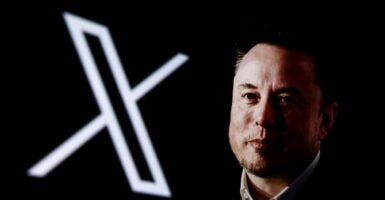 Elon Musk is posing next to the X logo, what he rebranded Twitter after he bought it.