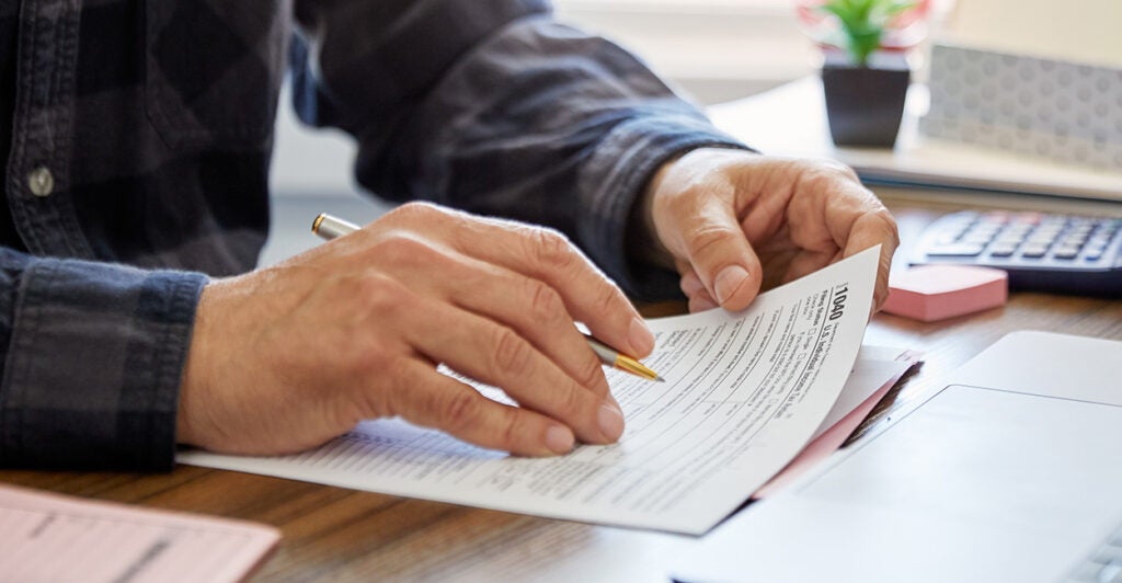 Close-up of a man holding a tax form, working from home. (Thanasis/Getty Images)