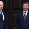 President Joe Biden waves to onlookers while he greets Chinese President Xi Jinping before a meeting. Both men are dressed in dark suits and dark ties.