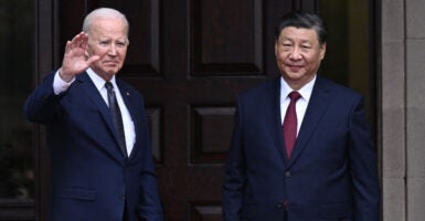 President Joe Biden waves to onlookers while he greets Chinese President Xi Jinping before a meeting. Both men are dressed in dark suits and dark ties.