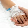 Child's hand with IV drip is held by an adult's hand.