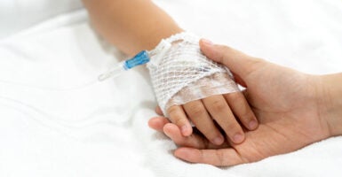 Child's hand with IV drip is held by an adult's hand.