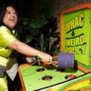 A lady in a green dress holds a mallet in her hand as she plays "Whac-A-Weird-Policy."