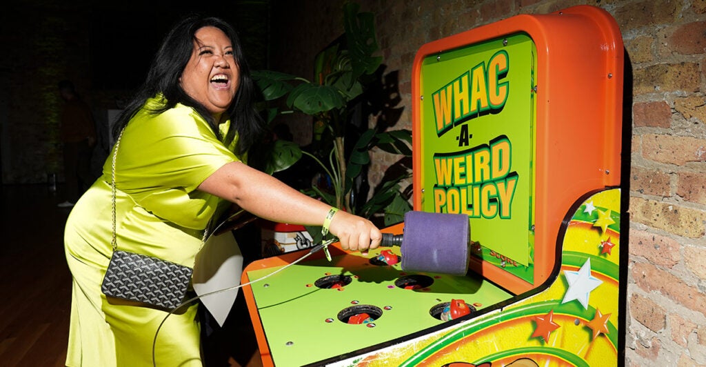 A lady in a green dress holds a mallet in her hand as she plays "Whac-A-Weird-Policy."