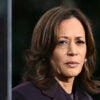 Kamala Harris in a dark purple suit, glancing to the side with a troubled expression on her face.