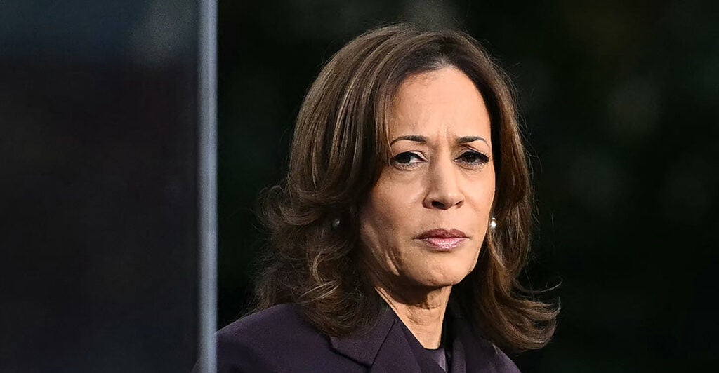 Kamala Harris in a dark purple suit, glancing to the side with a troubled expression on her face.