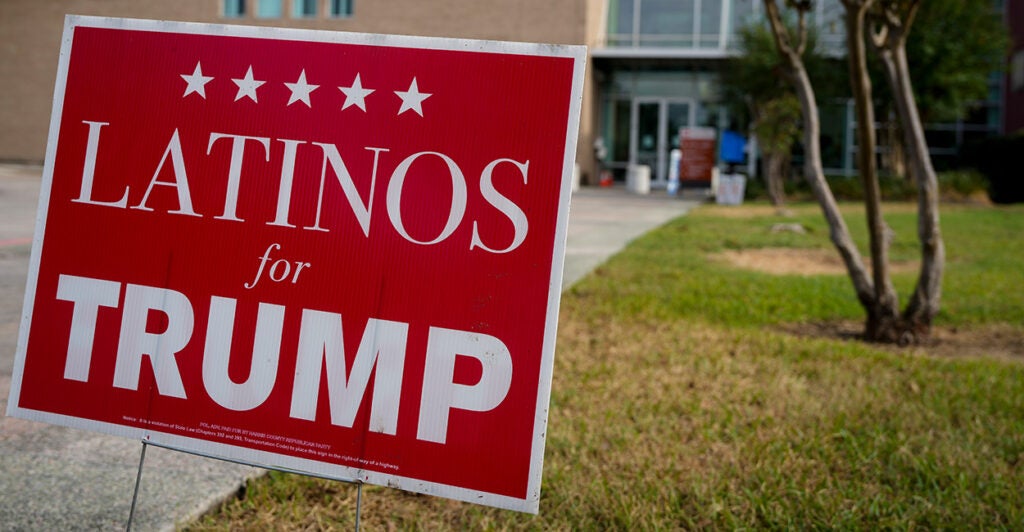 A red "Latinos for Trump" sign sits on the green grass outside a building.