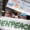 Climate activists from Greenpeace and Uplift stand together behind a large Greenpeace banner with white flowers in their hands during a demonstration outside the Scottish Court of Session, Edinburgh.