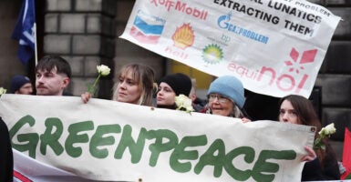 Climate activists from Greenpeace and Uplift stand together behind a large Greenpeace banner with white flowers in their hands during a demonstration outside the Scottish Court of Session, Edinburgh.