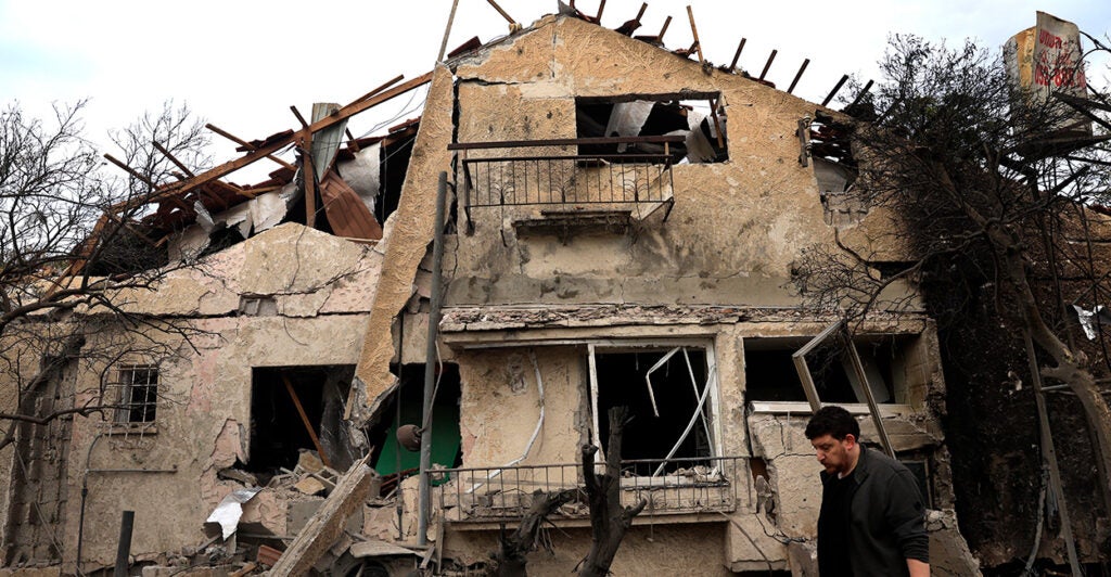 a man in a black shirt walks by a house destroyed by a missile attack in Israel