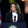 Kamala Harris in a white shirt and a black suit coat in front of American flags