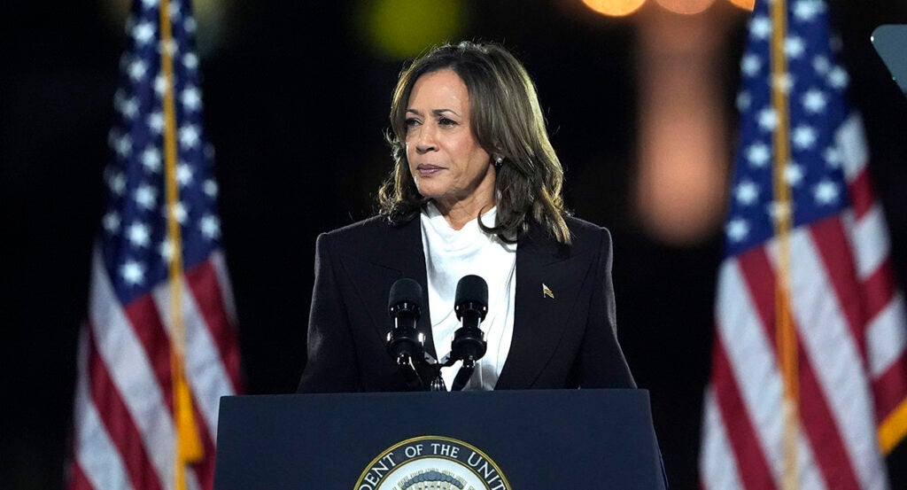 Kamala Harris in a white shirt and a black suit coat in front of American flags