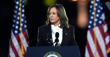 Kamala Harris in a white shirt and a black suit coat in front of American flags