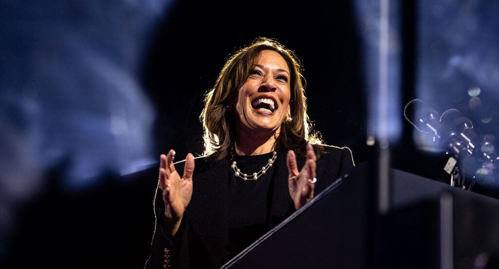 Kamala Harris in a black outfit and pearls laughs and claps her hands