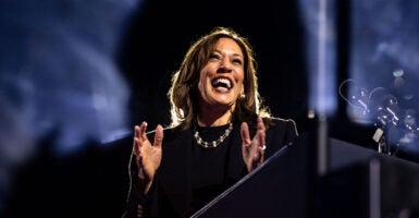 Kamala Harris in a black outfit and pearls laughs and claps her hands