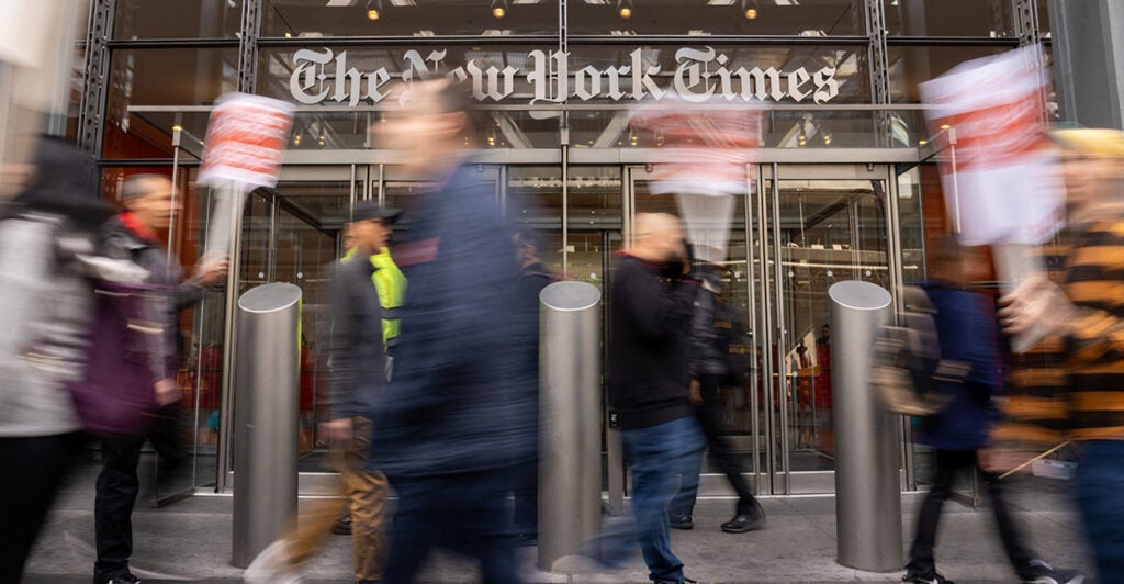 In front of The New York Times building, protestors hold signs.