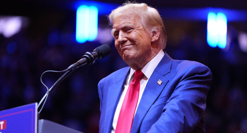 Donald Trump in a blue suit with a red tie smiles widely