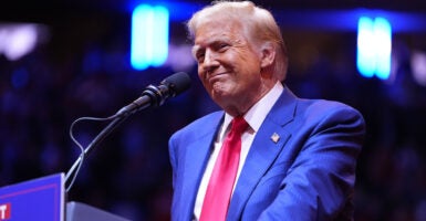 Donald Trump in a blue suit with a red tie smiles widely