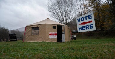 A “Vote Here” sign outside of a temporary voting site located in a tent in a wooded and grassy area