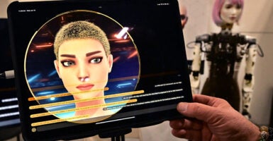 A female artificial intelligence character on a tablet screen with a humanoid robot on display in the background.