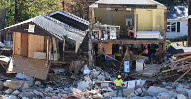 Destroyed homes sit on a rocky riverbed, a worker in neon helping with the clean-up effort.