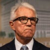 Los Angeles County District Attorney George Gascón in a dark suit and glasses with a frown talks to the media at a news conference