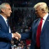 Robert F. Kennedy, Jr. and former President Donald Trump, both in dark blue suits, shake hands on stage at a Trump rally