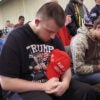 Man in Trump shirt holds a MAGA hat to his chest as he prays at a rally for President-elect Donald Trump.