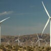 A field of large white windmills in the desert of Southern California against dark blue sky.