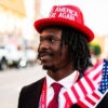 A black Trump supporter stands outside the Republican National Convention on July 17 wearing a red "Make America Great Again" hat and waving an American flag.