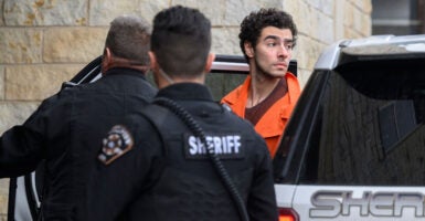 Luigi Mangione in an orange prison jumpsuit is led by police into an extradition hearing.