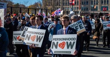 Pro-life protesters march down a street holding signs.