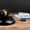 A judge's gavel lays on a desk next to a pile of money.