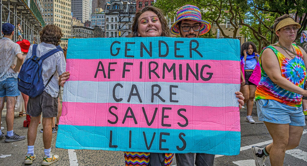 An activist holds a sign reading, "Gender-affirming care saves lives."