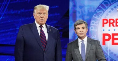 Donald Trump wears a navy blue suit as he poses next to George Stephanopoulos, wearing a grey suit.