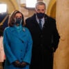 Nancy Pelosi wears a blue coat and black mask as she stands next to her husband, Paul Pelosi, who wears a black coat and black mask.