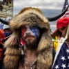 Jacob Chansley, dubbed "the QAnon Shaman,” has his face painted in red, white, and blue, as he wears a fur headdress with a horn on each side.