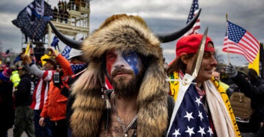 Jacob Chansley, dubbed "the QAnon Shaman,” has his face painted in red, white, and blue, as he wears a fur headdress with a horn on each side.