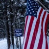 Along a wintery highway, an American flag hangs nailed to a snow-covered tree among pro-Trump campaign signs supporting the building of a border wall.