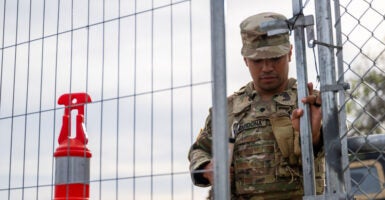 A black National Guard soldier dressed in a camouflage uniform pulls a silver-wired security gate closed.