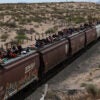 Migrants ride on top of freight cars.