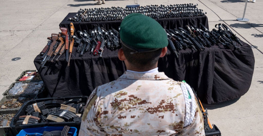 A Mexican soldier stands in front of guns.