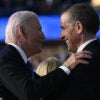 President Joe Biden and his son Hunter Biden, both dressed in black suits, smile at each after sharing a hug.